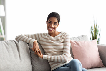 Young Happy African American Housewife Sitting On Couch In Living Room
