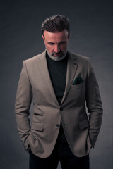 Fototapeta premium Portrait of a stylish elegant senior businessman with a beard and casual business clothes in photo studio isolated on dark background gesturing with hands