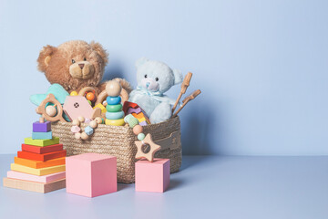 Toy box full of baby kid toys. Container with teddy bear, wooden rattles, stacking pyramid and wood blocks on light blue background. Cute toys collection for small children. Donatation. Front view