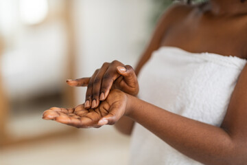 Cropped view of young black woman applying moisturizing hand cream at home, closeup