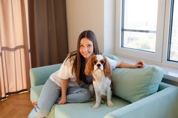 Young woman sitting at home on sofa with Cavalier King Charles Spaniel dog.