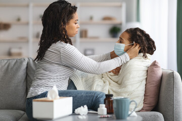 Black mother putting face mask on her sick little daughter