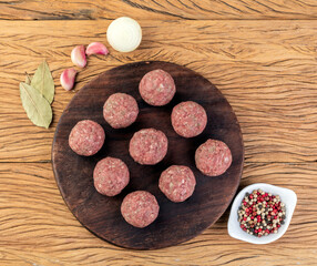 Raw meat balls over wooden board with seasonings