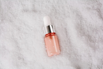 Cosmetic bottle with beauty product in the snow. Liquid skin or hair care product. Christmas and holiday concept. Top view and copy space
