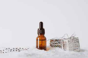 Serum glass bottle in the snow with christmas decoration: gift boxes on a white background. Liquid...