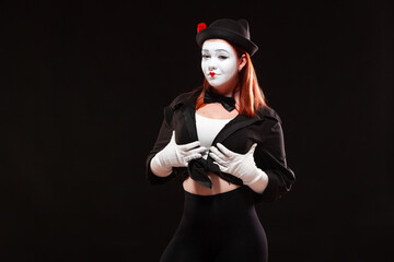 Portrait of female mime artist performing, isolated on black background. Woman touches her breast with confident look. Symbol of breast augmentation, big size