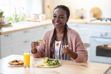 Cheerful Black Lady Eating Tasty Breakfast Or Lunch In Kitchen At Home