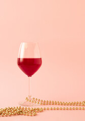 Golden pearls and glass of red wine against pastel pink background. Minimal New year celebration or still life concept.