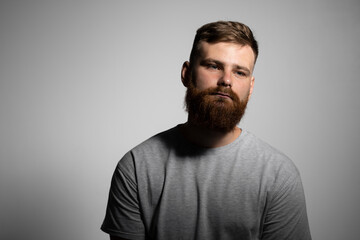 Fototapeta premium Close-up portrait of a handsome a brunette brutal bearded man in a grey t-shirt. Stylish and handsome man with a beard.
