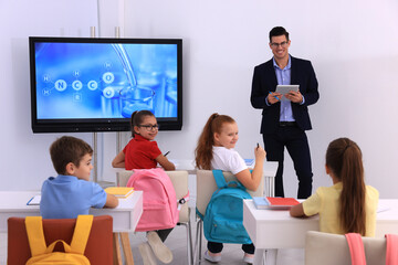 Teacher giving lesson to pupils near interactive board in classroom