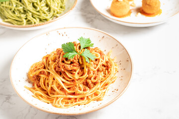 Delicious dishes of Italian gastronomy on white marbled board and gray background. Pasta bolognese, Arancini Siciliana, spaghetti with pesto. Copy space. High quality photo