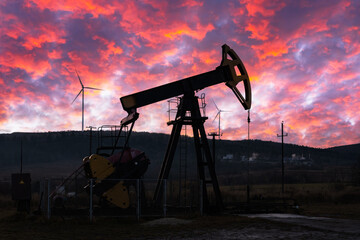 Oil pump and wind turbines against incredible purple sunset sky. Industrial concept