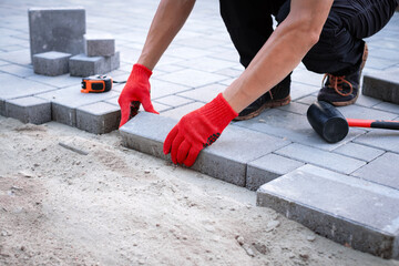The master in yellow gloves lays paving stones in layers. Garden brick pathway paving by...