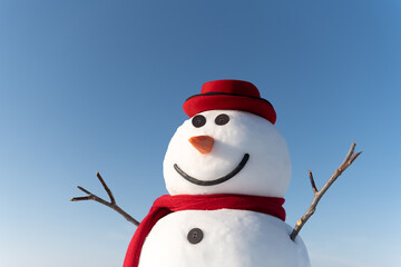 Funny snowman in stylish red hat and red scalf on snowy field. Blue sky on background