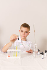 a white boy in a white coat conducts a chemical experiment. The boy prepares paints