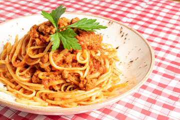 Tasty classic Italian spaghetti with bolognese and basil on a white plate on a red and white checkered tablecloth. Copy space for your text. High quality photo