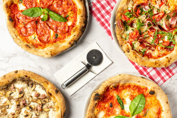 Top view of various types of pizza: Pizza with Prosciutto, Pizza with mushroom, Pizza with salami, ready to be cut with the cutting tool, on a white background and red checkered tablecloth.