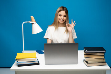 Happy woman using laptop and showing ok sign to a friends, colleagues or to a clients that everything is ok and looking in a computer screen.