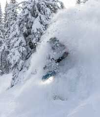 elite sports snowmobiler rides and jumps on steep mountain slope with swirls of snow storm. a trail of splashes of white snow. bright snowmobile and suit without brands