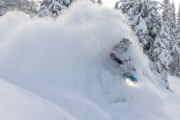 elite sports snowmobiler rides and jumps on steep mountain slope with swirls of snow storm. a trail of splashes of white snow. bright snowmobile and suit without brands