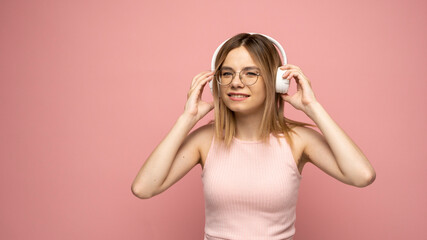 Beautiful young blonde woman with headphones and mobile device listening to music and smiling and dancing, isolated on pink background.