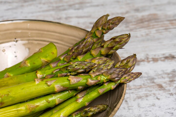 Raw asparagus in bowl on wooden desk