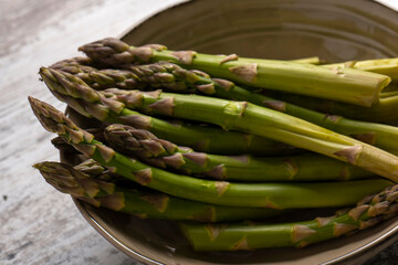 Raw asparagus in bowl on wooden desk