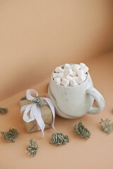 a cup of coffee with marshmallows on beige as minimal christmas background with a small gift box