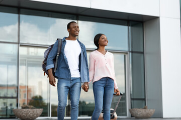 Happy Arrival. Portrait Of Cheerful Black Couple Leaving Airport Building With Luggage