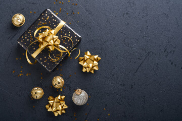 Holiday gift box or present with ribbon, golden confetti and gold baubles on black background. Magic christmas greeting card. Christmas Decoration. Border design. Mock up. Top view.