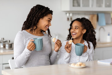 Cute black mother and daughter drinking tea with cookies