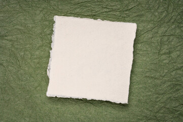 small square sheet of blank white Khadi paper against green textured paper