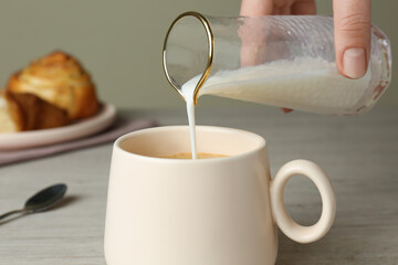 Woman pouring milk into cup of coffee at table, closeup
