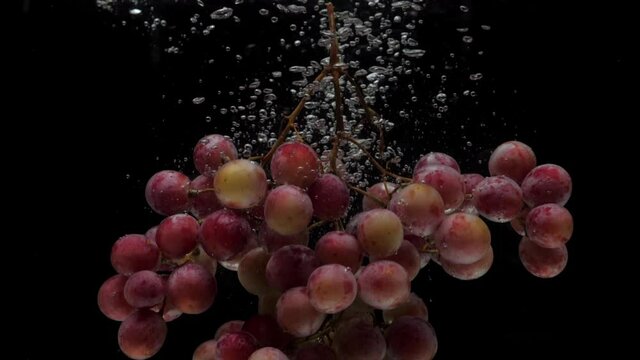 Slow motion red grapes falling into transparent water on black background. Fresh fruit splashing in aquarium. Healthy food, diet, air bubbles