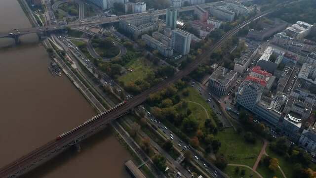 High angle view of traffic in city. Tracking of passenger train running on track across busy waterfront road and Vistula river. Warsaw, Poland
