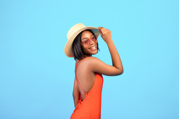 Summer fun. Portrait of cool black lady in stylish sunglasses, straw hat and bikini posing over blue background