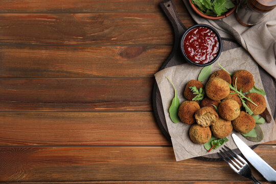 Delicious falafel balls with herbs and sauce served on wooden table, flat lay. Space for text