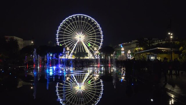 People attend Christmas decorations and coloured water fountains with the Ferris wheel in Nice, France