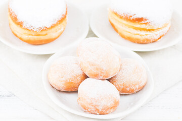 Donuts with powdered sugar and cream in saucers with a kitchen napkin on a white wooden table.