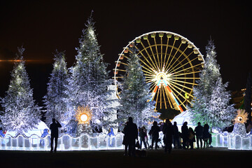 People watch Christmas decorations with snow-covered trees and funfair Ferris wheel. Nice, France