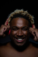 Black man in red wireless headphones looks at the camera and smiles on a black background