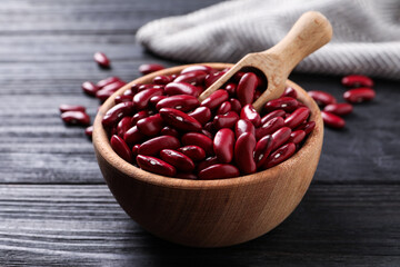 Raw red kidney beans in bowl and scoop on dark wooden table, closeup