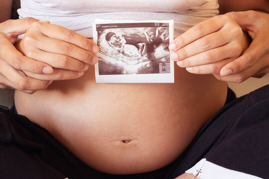 The image of beautiful pregnant woman and her husband holding her hands in a heart shape on her baby bump.