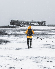 Person with a backpack walking towards a plane wreck during the heavy snowfall