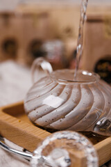 Glass teapot on a blackboard against the background of tea packaging. Boiling water is poured into...