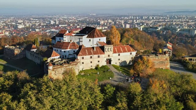 Aerial drone view of The Citadel in Brasov at sunrise, Romania. Medieval fortress on the top of a hill. Buildings, yellowed trees, tourists