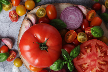 Flat lay composition of different tomatoes, onion, basil and garlic	