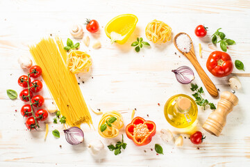 Italian food frame on white kitchen table. Raw Pasta, olive oil, spices, vegetables and basil. Top view with copy space.