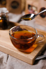 Hand, stirring sugar in a mug of tea. A wooden board, pieces of chocolate and a candle.