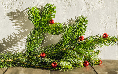 Fototapeta na wymiar Fir branch with small red christmas balls on the rustic background in sunshine day.